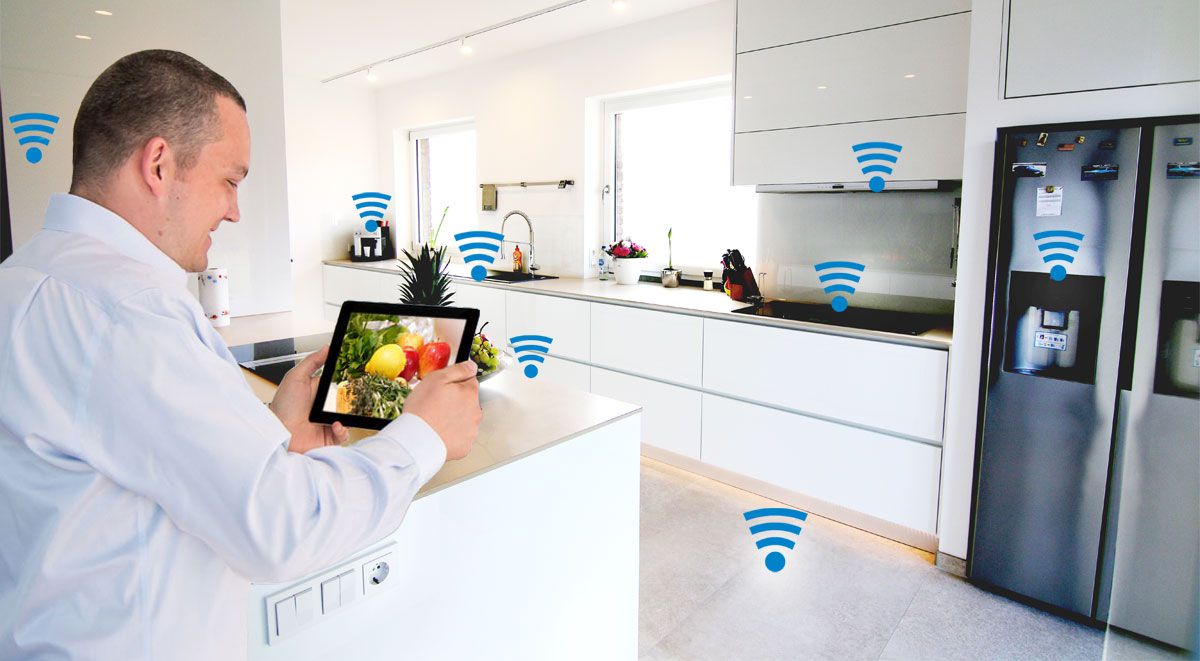 Mann in einer modernen Küche, der ein Tablet benutzt, um das smarte Kühlschrank- und Haushaltsgeräte-Ökosystem zu steuern, symbolisiert durch die Wi-Fi-Icons.
